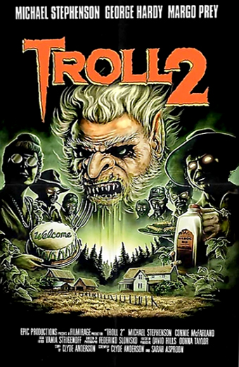 Locandina di Troll 2 con due creature simili a goblin dagli occhi luminosi, una tiene una bottiglia con la scritta Nilbog Milk e l'altra un cartello con scritto Welcome. Sullo sfondo si vede un villaggio rurale con case e alberi sotto un cielo drammatico. In alto il titolo Troll 2 in grandi lettere arancioni, sopra i nomi Michael Stephenson, George Hardy e Margo Prey. Il tono generale è inquietante e surreale.