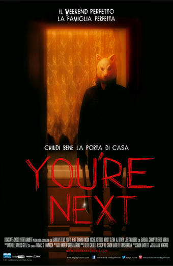 Locandina del film Youre Next con una figura in silhouette scura che indossa una maschera animale e sta in piedi in una porta con tende arancioni. La locandina contiene testo in italiano: Il weekend perfetto, la famiglia perfetta; Chiudi bene la porta di casa; Youre Next in grandi lettere rosse. Il tono generale è di suspense e inquietudine.